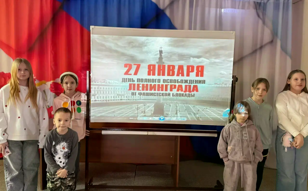 дети стоят на сцене там прожектор где написано 27 января день освобождения ленинграда.png